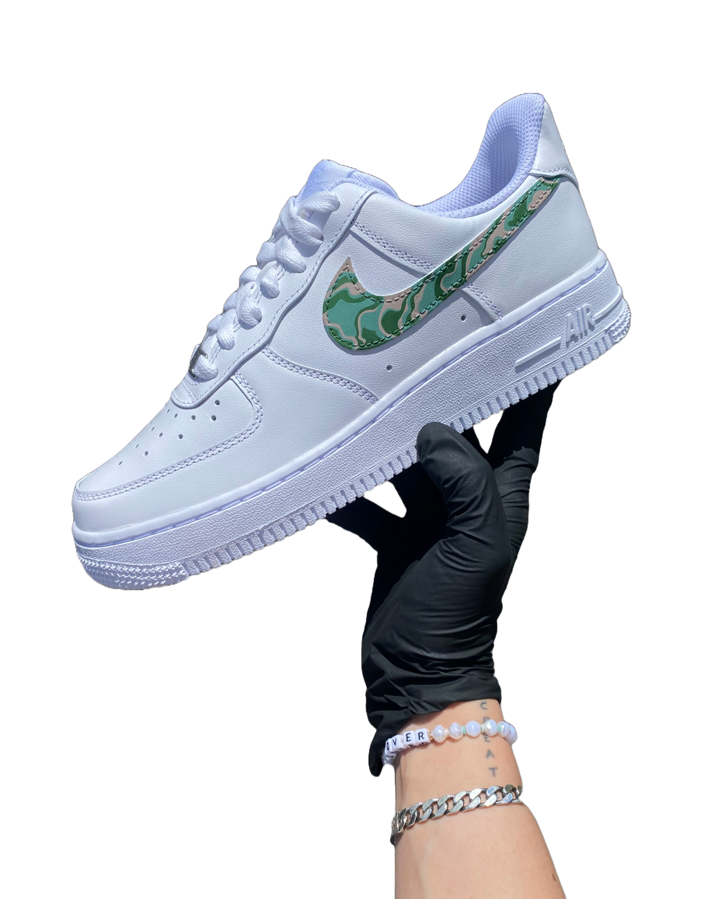 Artist's hand holding hand-painted spiral design on what would otherwise be a white pair of Air Force 1's. Colors include moss green, forest green and biege. Angle 1.