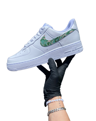 Artist's hand holding hand-painted spiraldesign on what would otherwise be a white pair of Air Force 1's. Colors include moss green, forest green and biege. Angle 2.