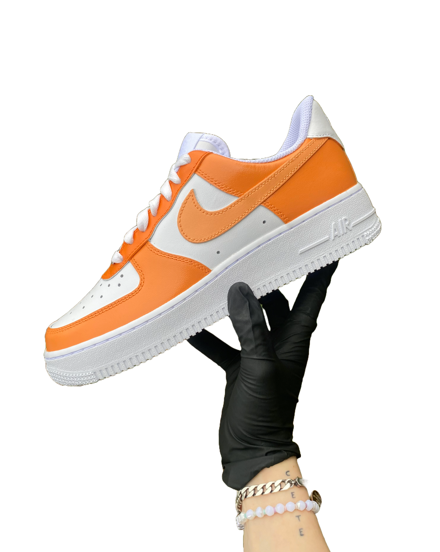 Artist's hand holding hand-painted orange colorway Air Force 1. There are 3 shades of orange worked into the colorway. Angle 1.