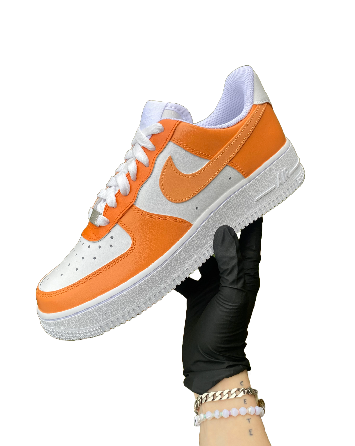 Artist's hand holding hand-painted orange colorway Air Force 1. There are 3 shades of orange worked into the colorway. Angle 1.
